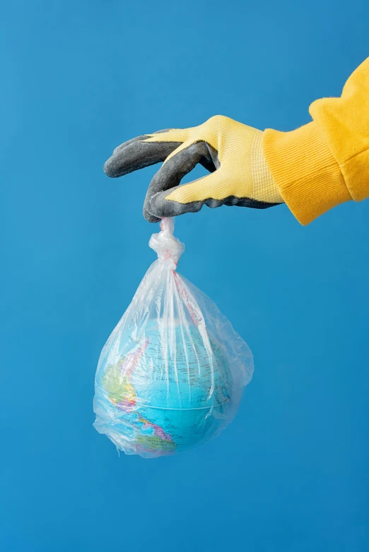 a person holding a bag of garbage on a blue background, by Dan Content, plasticien, large globe, yellow latex gloves, 8, contain