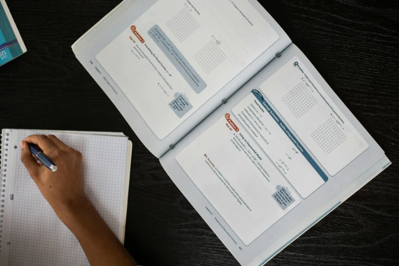 a person writing in a notebook on a table, danube school, detailed product image, fan favorite, charts, holding a giant book