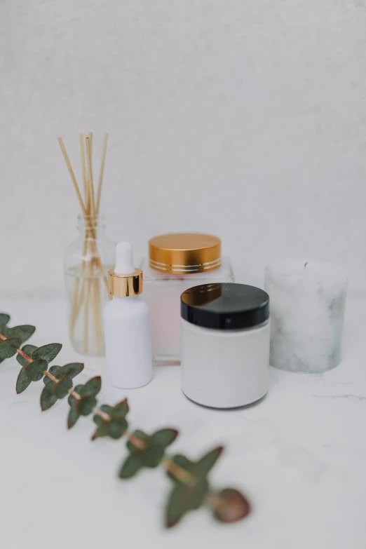 a white table topped with bottles and candles, pexels, photoshoot for skincare brand, detailed product image, jar on a shelf, gold