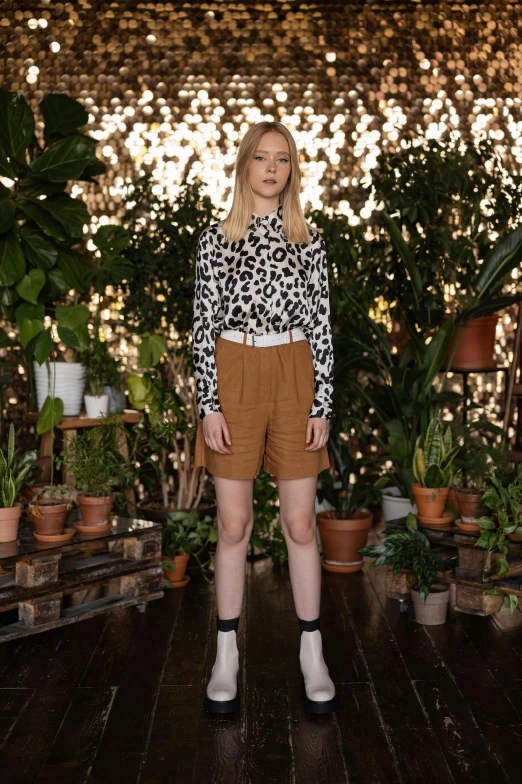 a woman standing in a room filled with potted plants, a portrait, trending on pexels, renaissance, wears shorts, brown shirt, britt marling style 3/4, wearing animal skin clothing