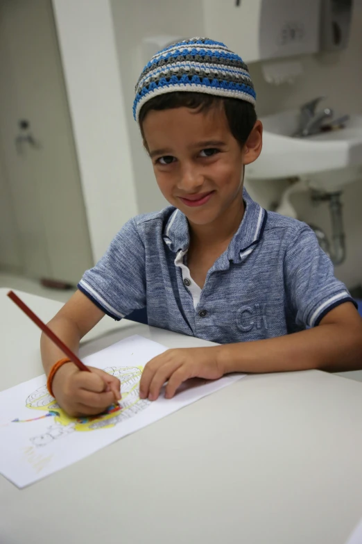 a young boy sitting at a table with a pencil and paper, by Zahari Zograf, colouring - in sheet, ahmad merheb, subject is smiling, still of rainbow ophanim