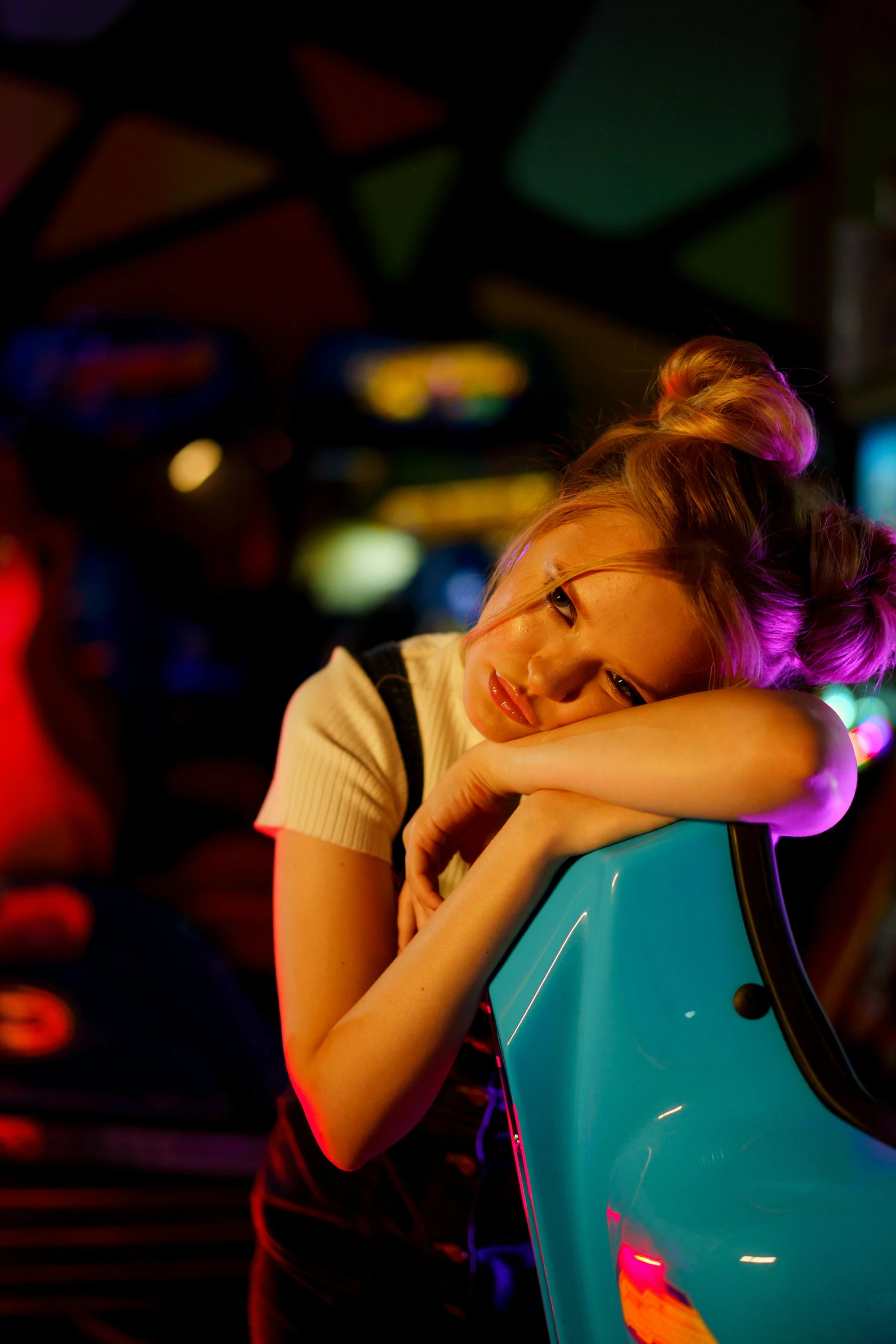 a young girl sitting on top of a blue car, inspired by Nan Goldin, pexels, sitting alone at a bar, a busy arcade, annasophia robb, sleepy expression