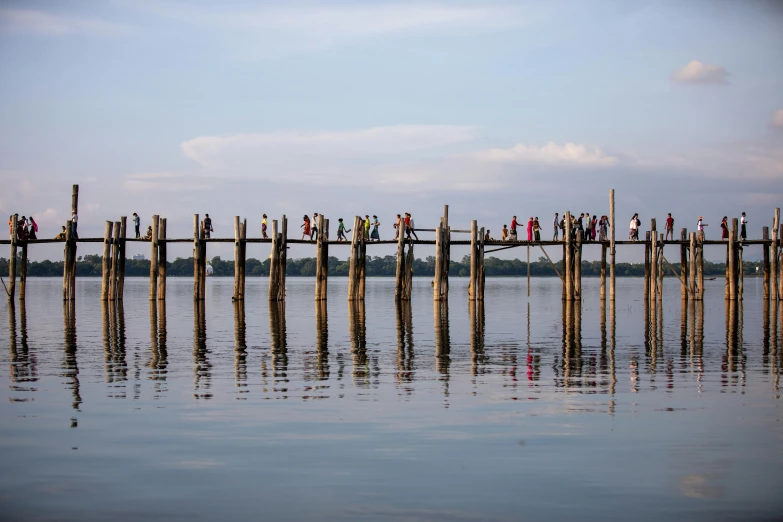 a group of people standing on top of a wooden bridge, inspired by Steve McCurry, pexels contest winner, hurufiyya, tall columns, myanmar, vine bridge silhouette over lake, 15081959 21121991 01012000 4k