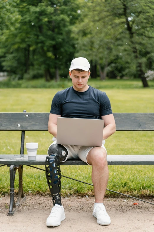 a man sitting on a bench with a laptop, prosthetic, non-binary, knee pads, parks