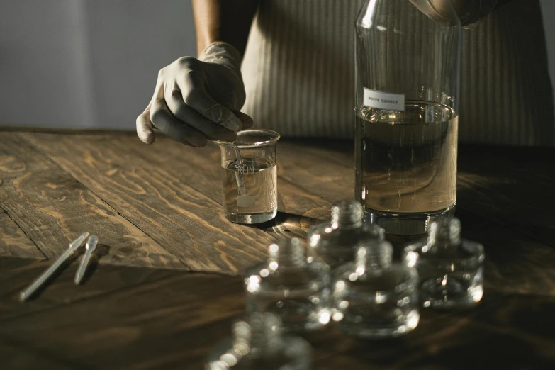 a person pouring water into a glass on a table, unsplash, process art, victorian alchemists, medical laboratory, bottle of vodka, transparent