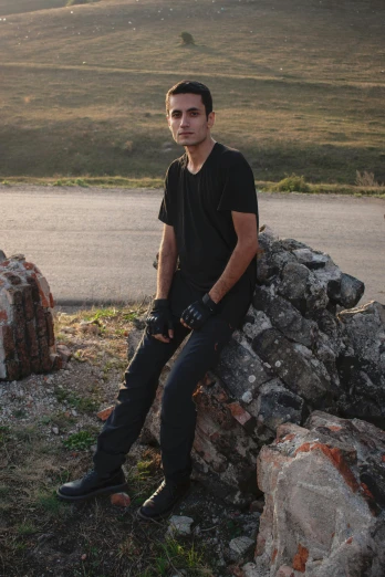 a man sitting on top of a pile of rocks, an album cover, inspired by Alexis Grimou, pexels contest winner, renaissance, wearing a dark shirt and jeans, standing in road, portrait of danny gonzalez, an edgy teen assassin