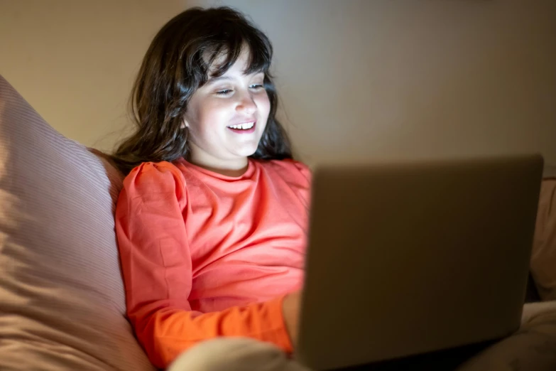 a little girl sitting on a couch using a laptop, pexels, orange glow, aged 13, avatar image, bottom angle