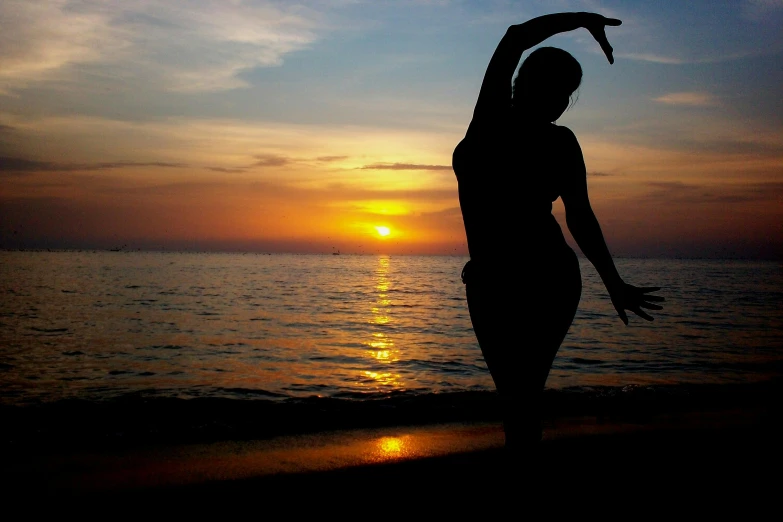 a woman standing on top of a beach next to the ocean, a picture, arabesque, golden hour in boracay, profile image, stretch, ((sunset))