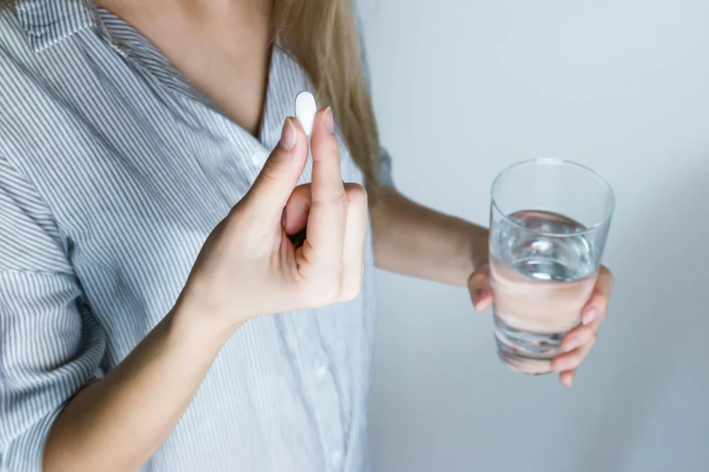 a woman holding a pill and a glass of water, unsplash, private press, holding a pudica pose, no skin shown, white, magnesium