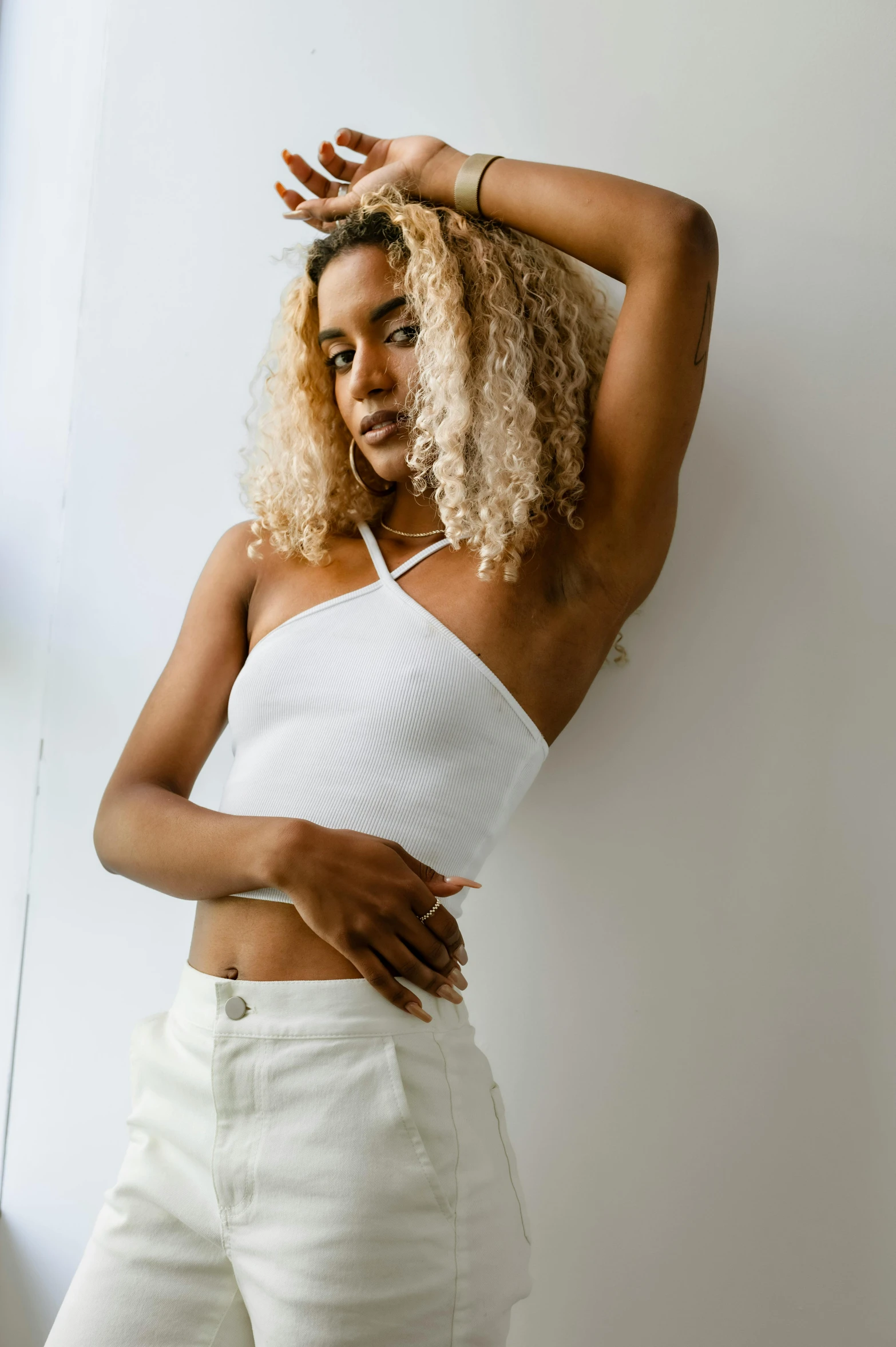 a woman with blonde hair leaning against a wall, by Dulah Marie Evans, trending on pexels, renaissance, white halter top, white pants, doja cat, on a white table