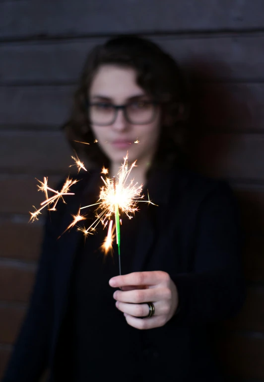 a woman holding a sparkler in her hand, by Niko Henrichon, girl with glasses, medium close-up, small, digitally enhanced