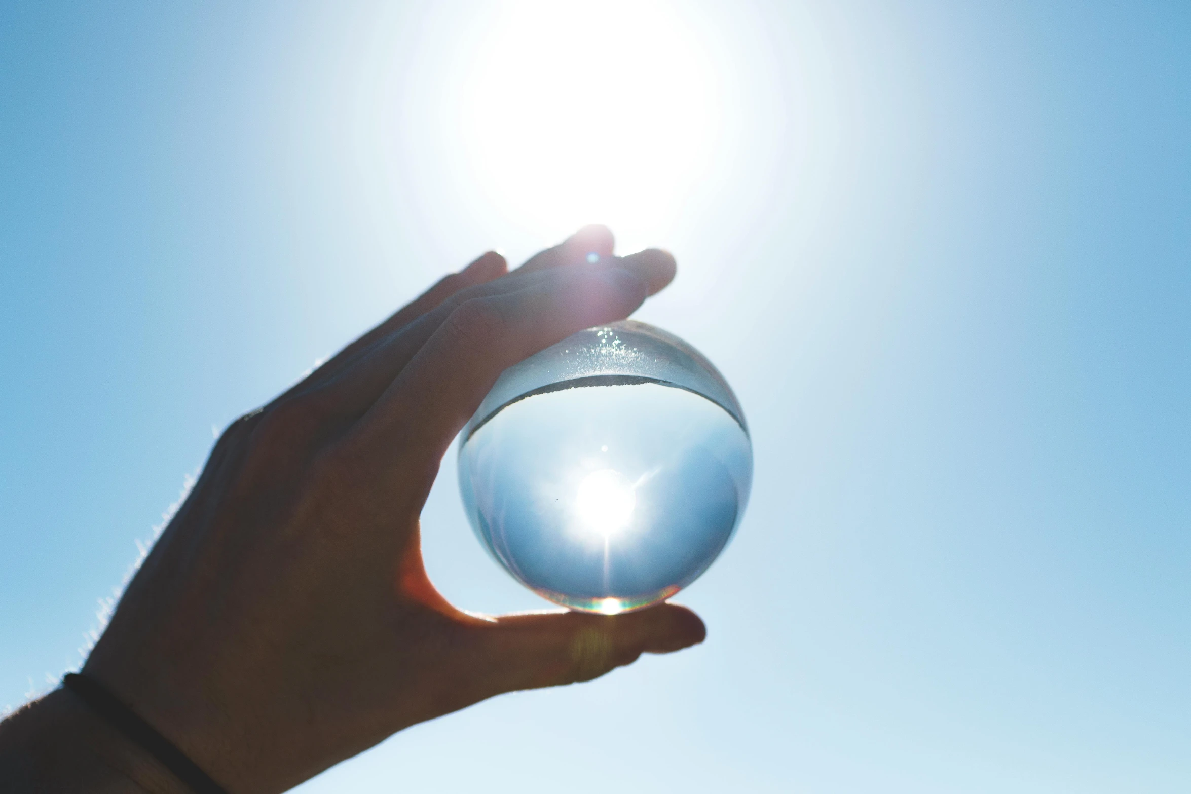 a person holding a glass ball in front of the sun, water element, clear blue skies, solarised, instagram post
