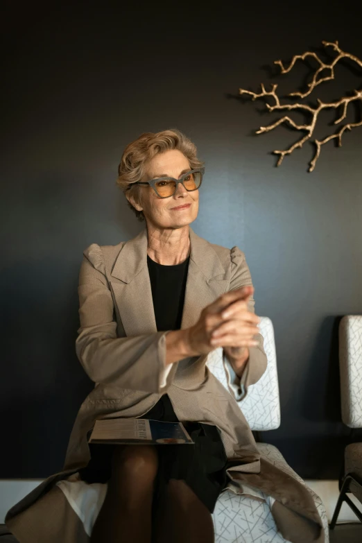 a woman sitting on a couch in a room, a portrait, unsplash, process art, in suit with black glasses, carmen dell ’ orefice, sitting on a mocha-colored table, professional profile photo