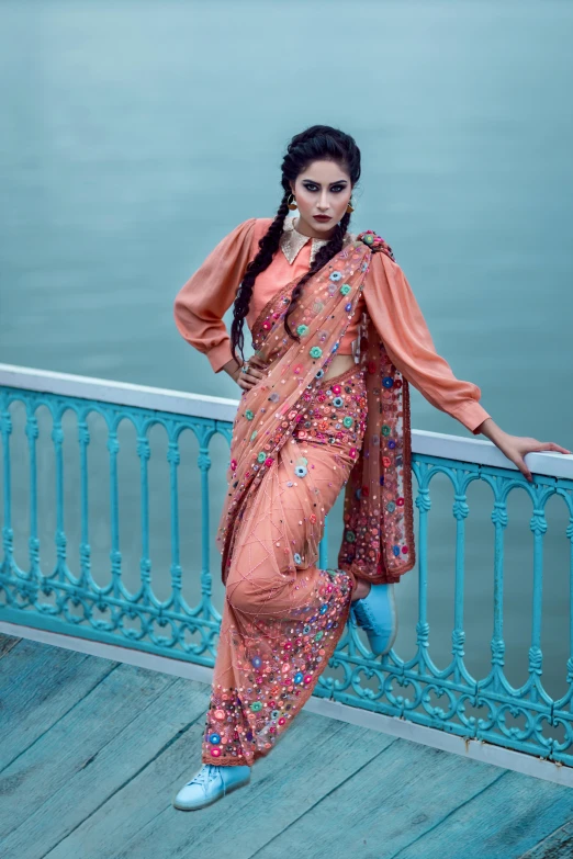 a woman standing on a bridge next to a body of water, baroque, wearing a steampunk sari, in shades of peach, fabric embroidery, promotional image