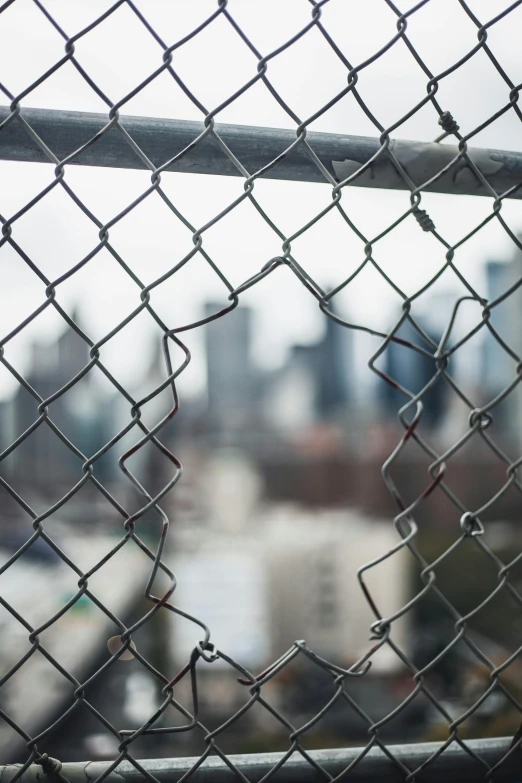 a view of a city through a chain link fence, an album cover, pexels contest winner, broken down, viral photo, body breaking apart, construction