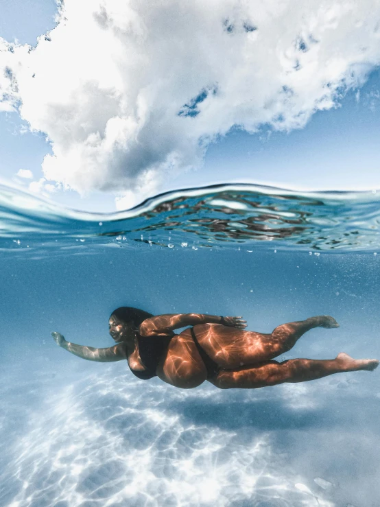 a woman in a bikini swims under the water, unsplash contest winner, full figured mother earth, big sky, dark-skinned, maternal photography 4 k