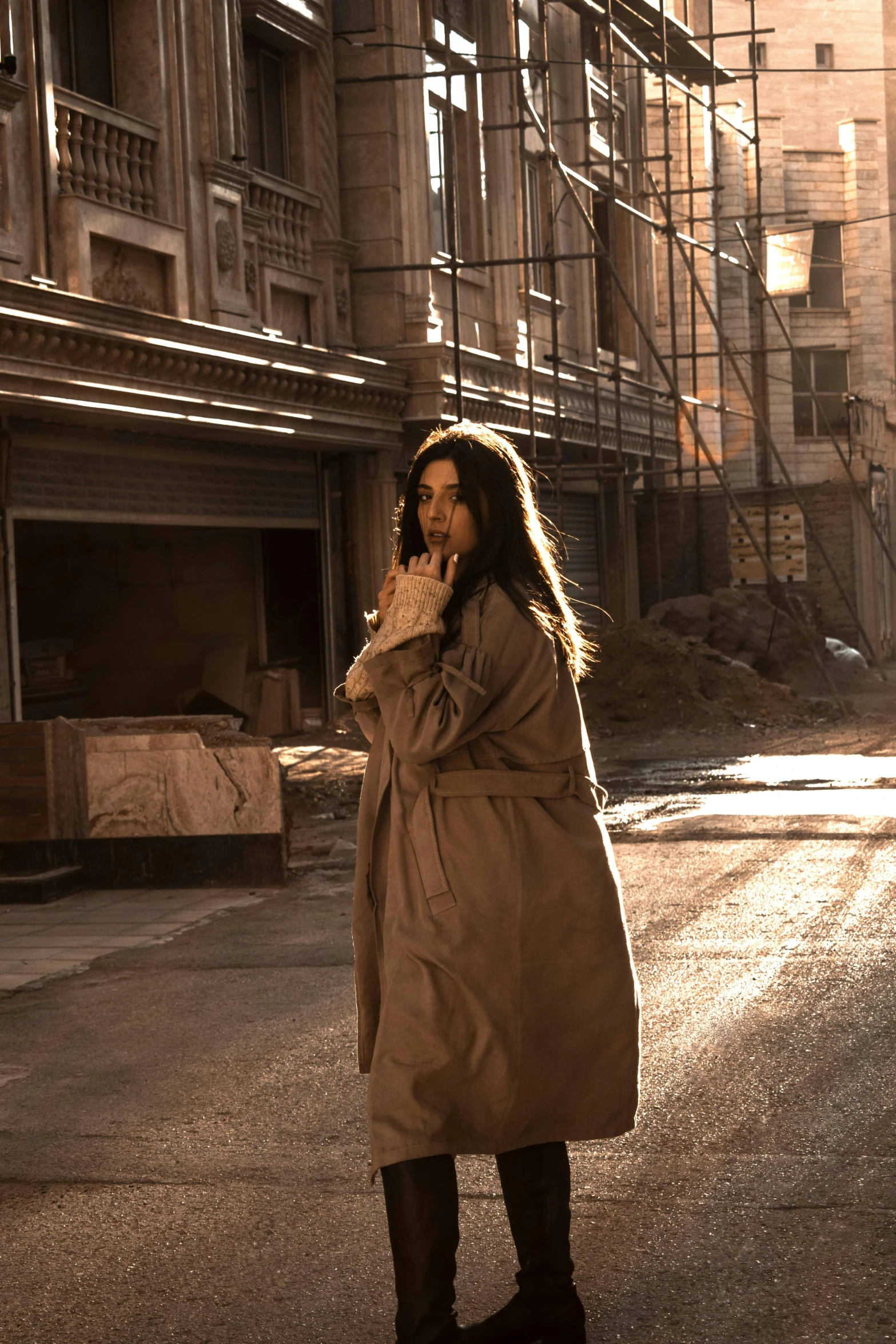 a woman standing in the middle of a street, inspired by roger deakins, pexels contest winner, light brown trenchcoat, in front of a ruined city, mahira khan as a mage, cinematic studio light! windy