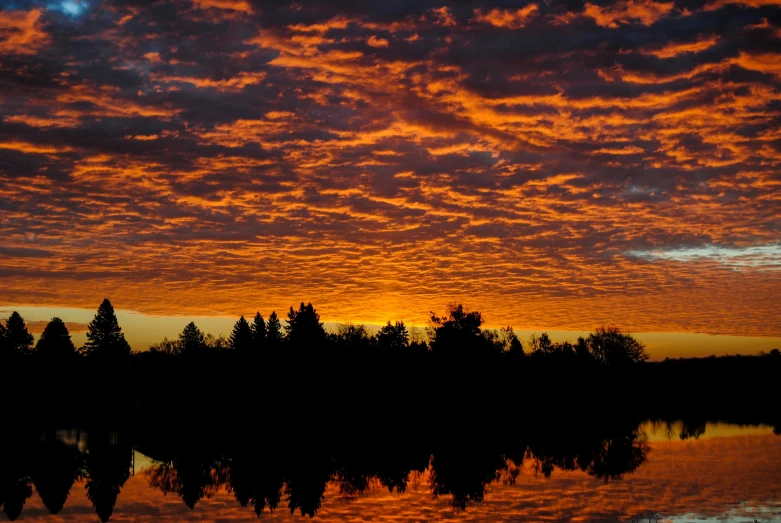a sunset over a body of water with trees in the background, orange clouds, award - winning photo ”
