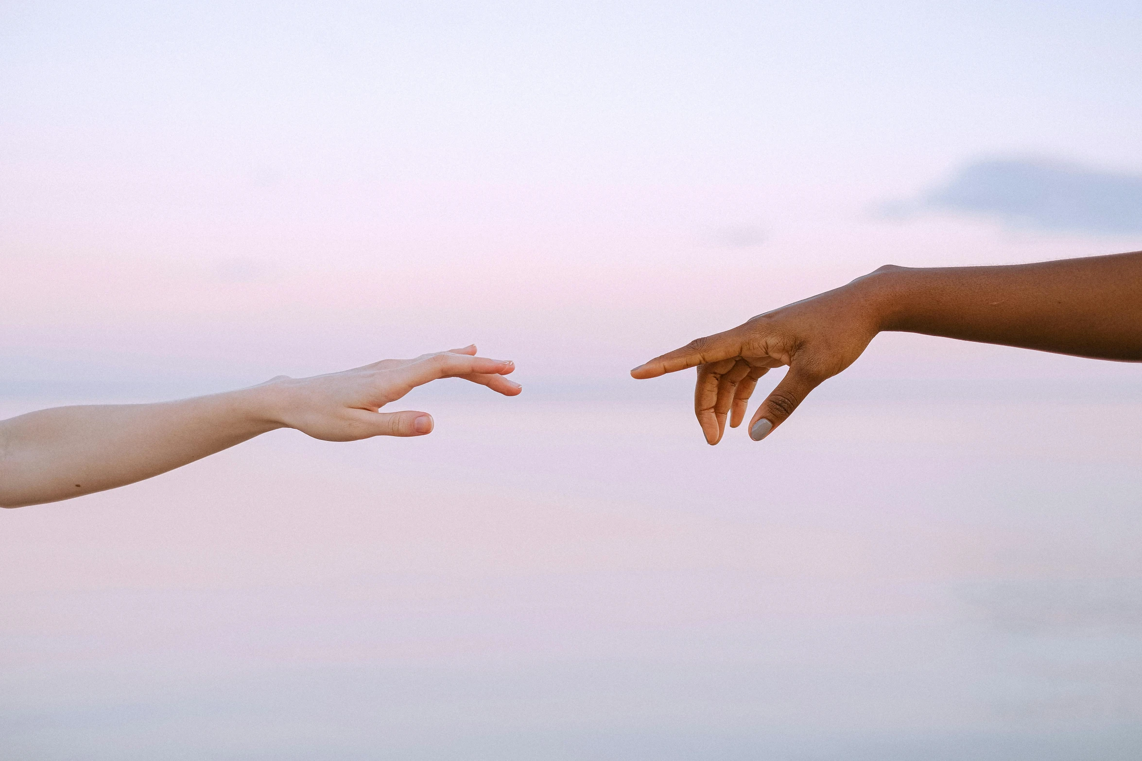 two hands reaching towards each other in front of a body of water, by Carey Morris, unsplash, varying ethnicities, pink golden hour, plain background, colour photograph