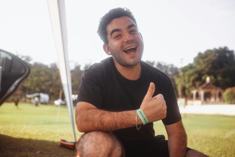 a man sitting on the ground giving a thumbs up, pexels contest winner, hurufiyya, manly, background : diego fazio, very slightly smiling, profile image