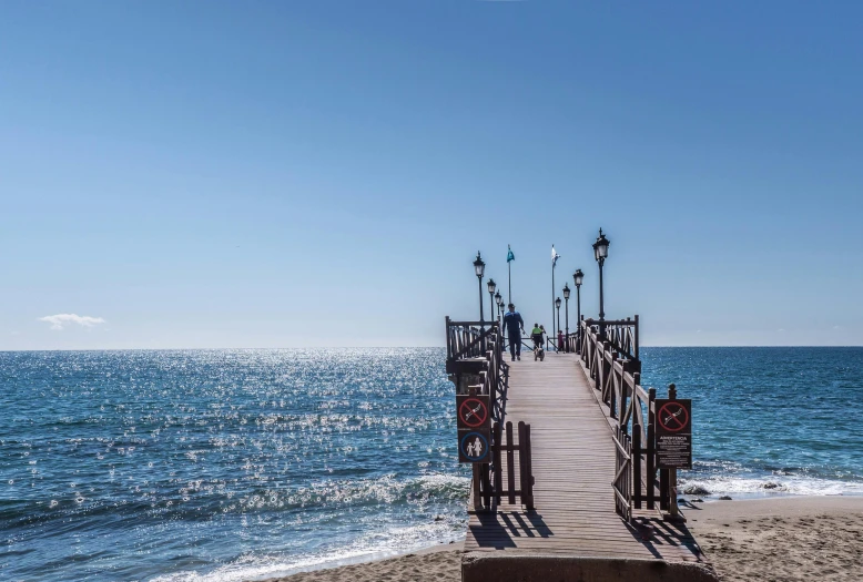 a pier sitting on top of a sandy beach next to the ocean, marbella, profile image