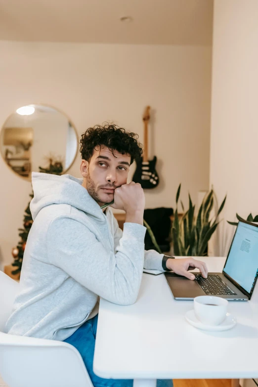 a man sitting at a table with a laptop, trending on pexels, happening, curly haired, non binary model, in white room, daniel ricciardo