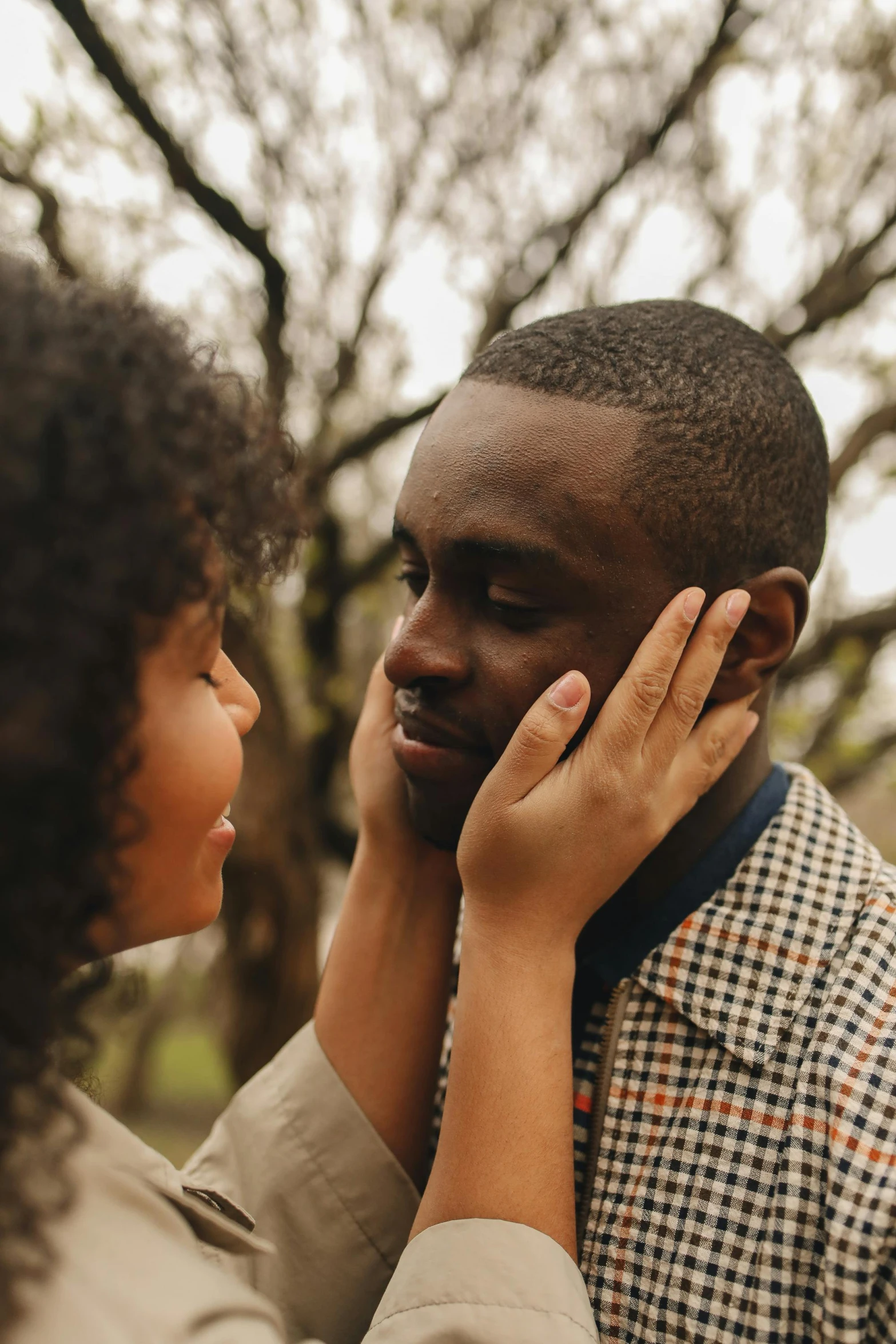 a man standing next to a woman in a park, trending on pexels, romanticism, african facial features, touching heads, hands shielding face, brown