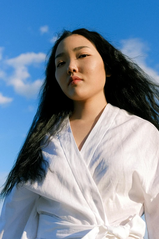 a woman with long black hair wearing a white robe, an album cover, inspired by Kim Tschang Yeul, unsplash, hyperrealism, blue skies, wearing a light shirt, lizzo, half asian