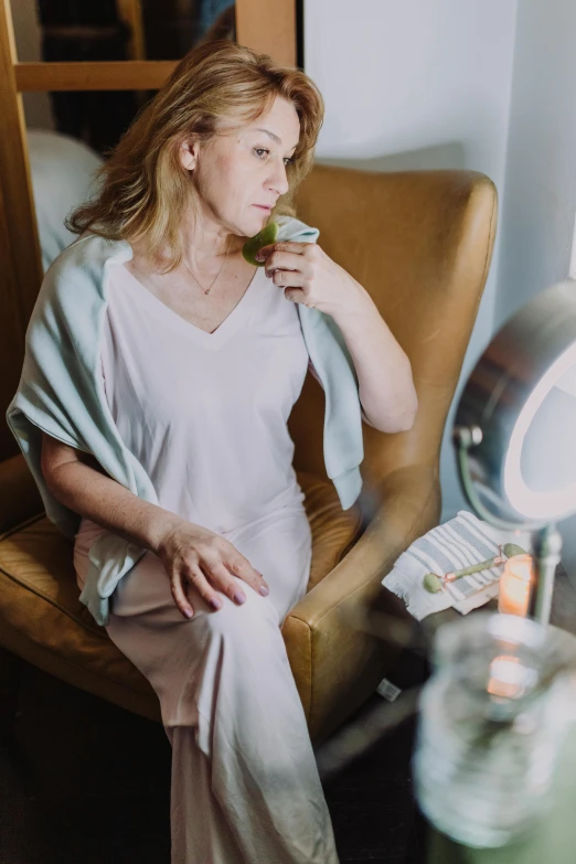 a woman sitting in a chair in front of a mirror, holding a drink, wearing nanotech honeycomb robe, loputyn and matcha, soft evening lighting