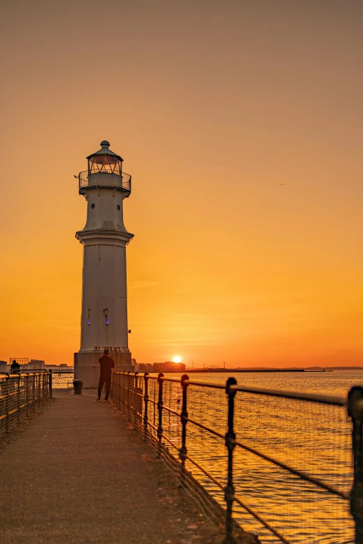 a lighthouse sitting on top of a pier next to the ocean, in the sunset, surrounding the city, hull, brightly-lit