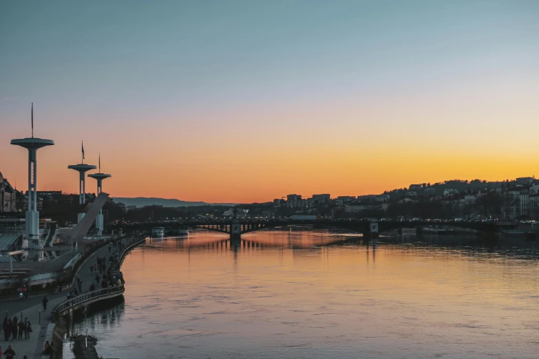 a large body of water with a bridge in the background, pexels contest winner, vista of a city at sunset, austro - hungarian, traveling in france, godrays at sunset