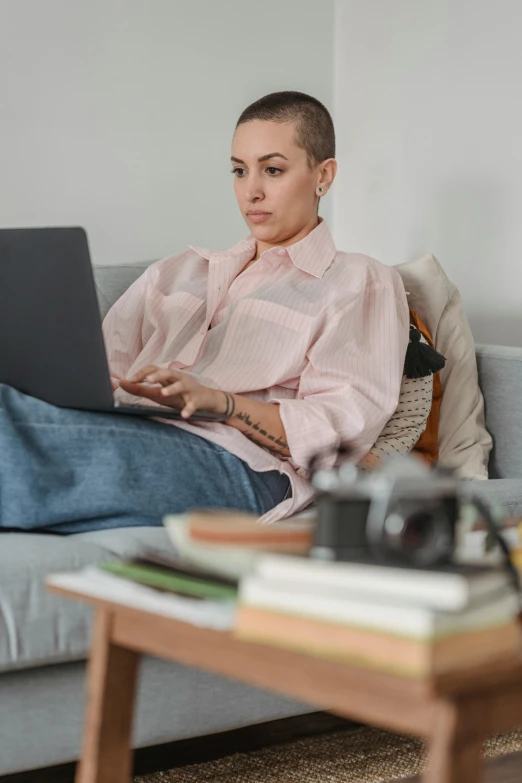 a woman sitting on a couch using a laptop, trending on pexels, renaissance, shaved head, office clothes, hunting, cover story