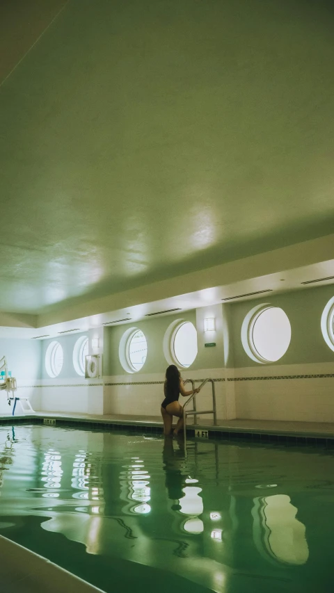 a woman sitting at the edge of a swimming pool, inspired by Elsa Bleda, unsplash, art nouveau, capsule hotel, low quality photo, indoor scene, portholes