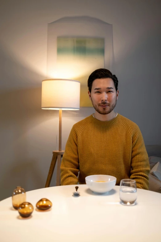 a man sitting at a table in front of a lamp, a portrait, unsplash, shin hanga, mark edward fischbach, ready to eat, sitting in bedroom, slightly smiling