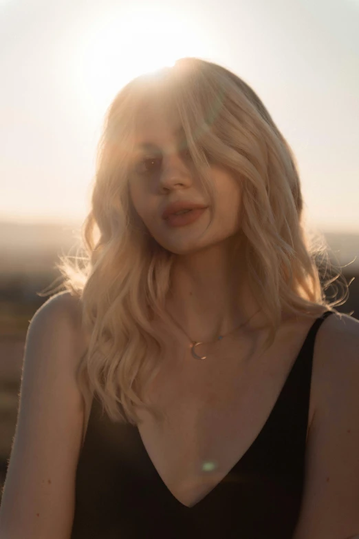 a woman in a black dress standing in a field, a picture, inspired by Elsa Bleda, trending on pexels, light gold hair, lucy in the sky with diamonds, neck zoomed in, sunstone