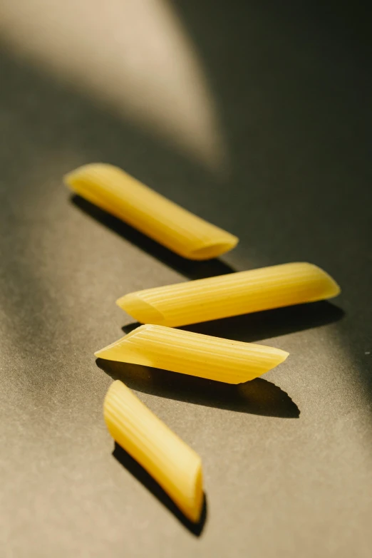 three pieces of pasta sitting on top of a table, sharp tip, lit from bottom, straight smooth vertical, it's getting dark
