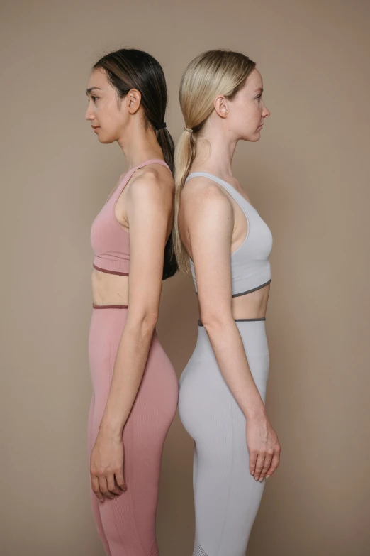 a couple of women standing next to each other, a colorized photo, inspired by Vanessa Beecroft, trending on pexels, renaissance, detailed sports bra, pink and grey muted colors, rotated left right front back, photoshoot for skincare brand