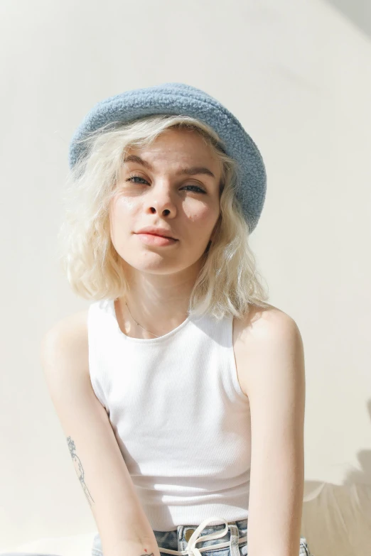 a woman sitting on a couch wearing a hat, inspired by Elsa Bleda, featured on reddit, short wavy blond hair, pale blue outfit, headshot photo, cloud hair