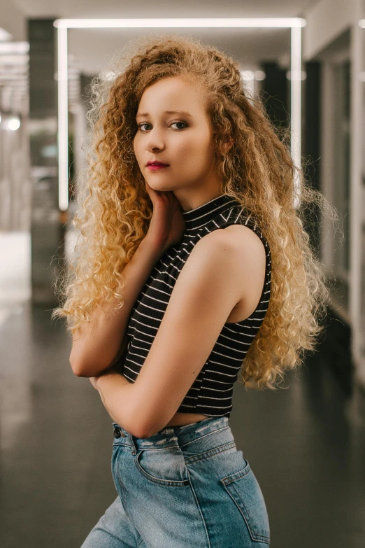 a woman with curly hair standing in a hallway, trending on pexels, long blonde or red hair, wearing a crop top, portrait photo of a backdrop, handsome girl