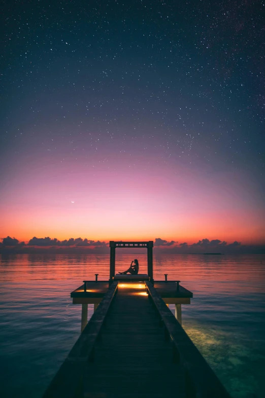 a person sitting on a dock at sunset, pexels contest winner, under a sea of stars, exotic endless horizon, faded glow, vacation photo