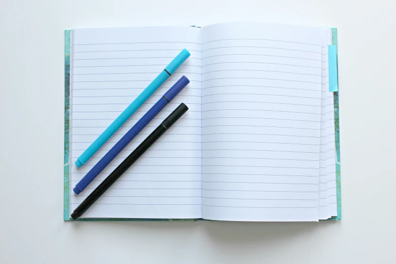a notebook with two pens on top of it, by Carey Morris, pexels, blue and green colours, lined up horizontally, black and aqua colors, wide screenshot