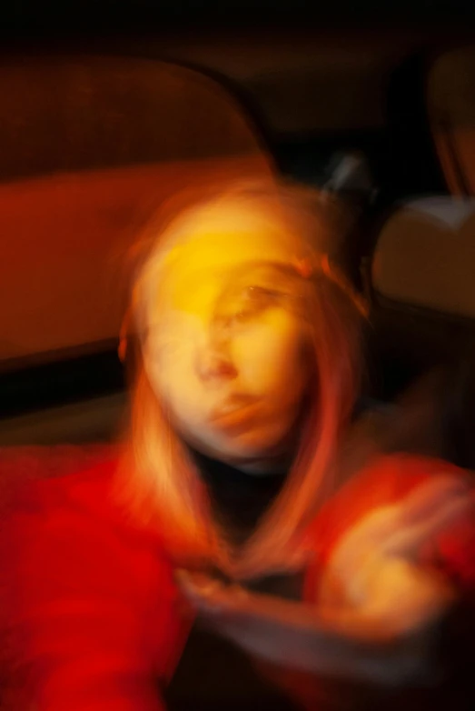 a blurry photo of a woman in a red shirt, inspired by Cindy Sherman, synchromism, red and yellow light, ava max, car shot, downward somber expression