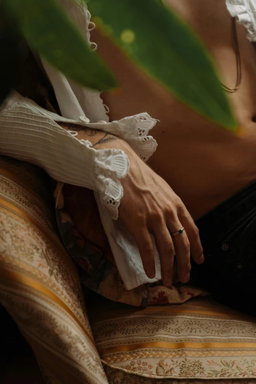 a woman sitting on top of a couch next to a plant, inspired by Elsa Bleda, trending on pexels, renaissance, photo of a hand jewellery model, white sleeves, slightly erotic, rococo details