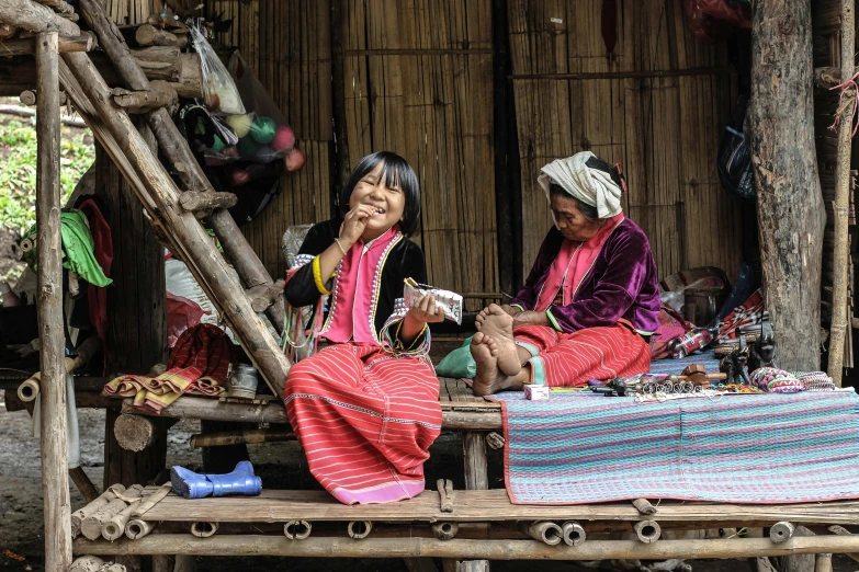 a couple of women sitting on top of a wooden bench, tribal clothing, weaving, patiphan sottiwilaiphong, avatar image