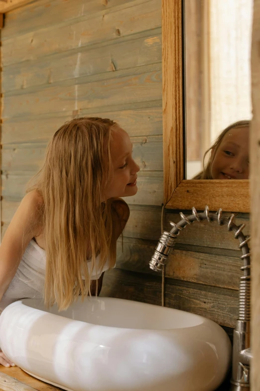 a woman washing her hands in a bathroom sink, a picture, inspired by Edwin Georgi, pexels contest winner, luxurious wooden cottage, young girl, looking into a mirror, glamping