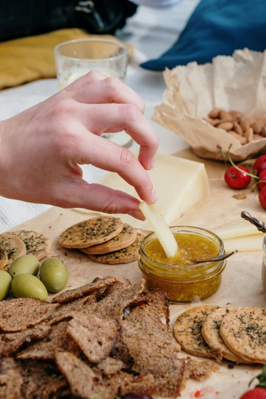 a wooden cutting board topped with crackers and olives, inspired by Ceferí Olivé, renaissance, hands, eating cheese, honey, medium level shot