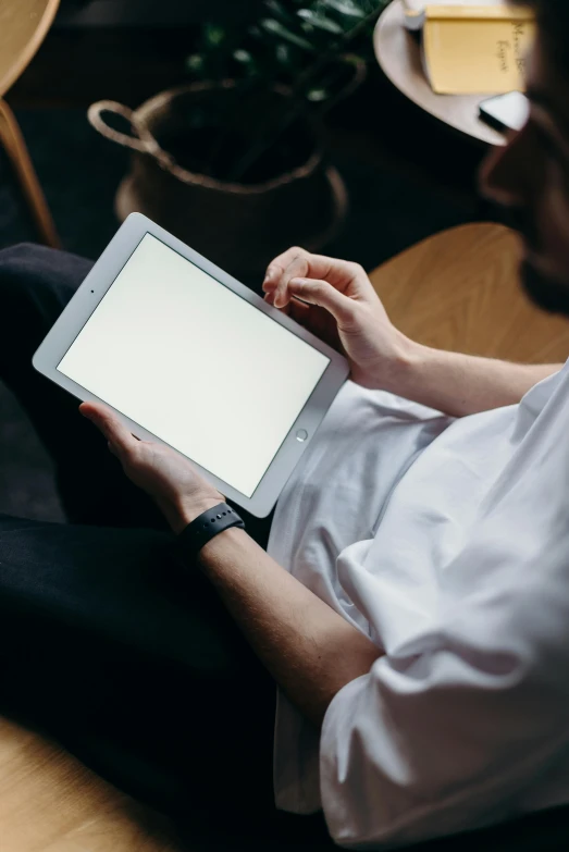 a man sitting on a couch using a tablet computer, trending on pexels, wearing a white shirt, a high angle shot, seated at a table, ilustration