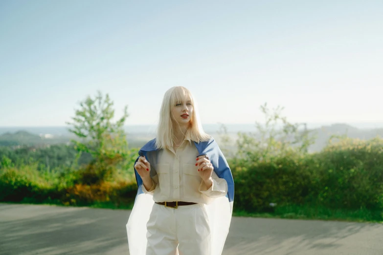 a woman in white pants and a blue jacket, an album cover, unsplash, albino white pale skin, hills in the background, wearing a cape, wearing lab coat and a blouse