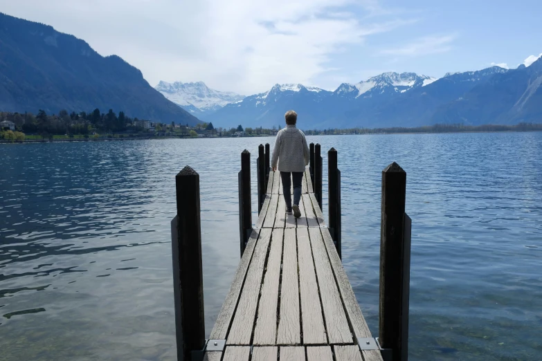 a man standing on a dock with mountains in the background, inspired by Peter Zumthor, pexels contest winner, visual art, walking away, today\'s featured photograph 4k, lakeside, classic gem