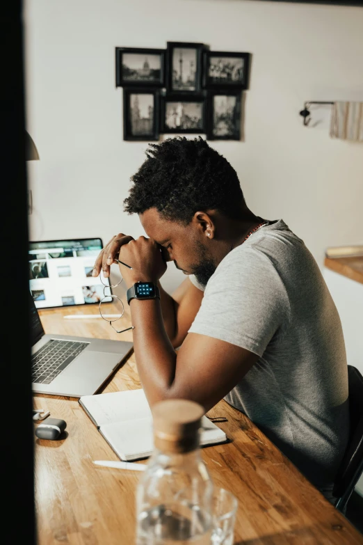 a man sitting at a table in front of a laptop computer, trending on pexels, renaissance, heartbroken, black man, busy room, praying